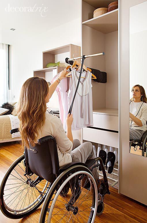 Persona en silla de ruedas cuelga ropa en su armario para personas con discapacidad.