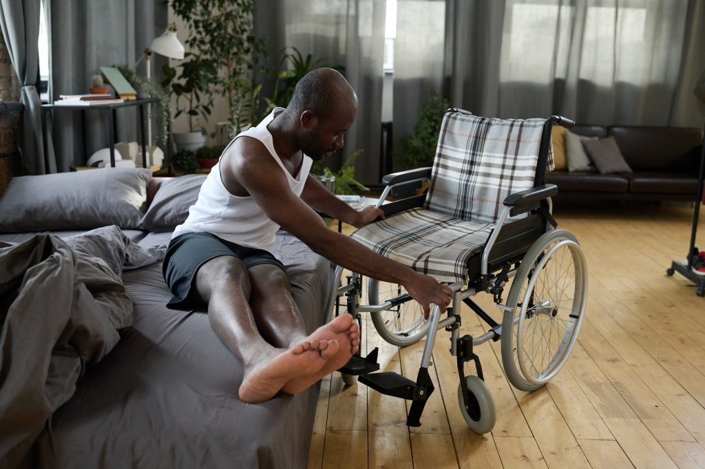Persona con discapacidad motriz alcanza su silla de ruedas desde la cama.